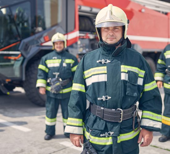 Waist up portrait of firefighter crew in protective fireproof uniform in front of fire engine machine